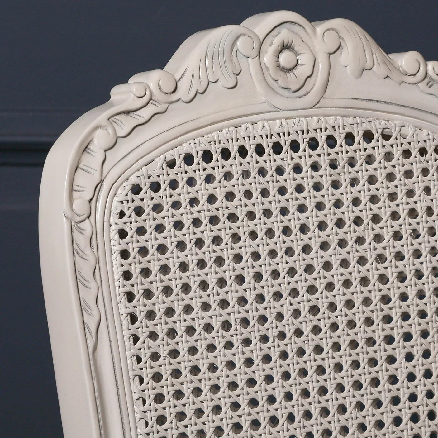 Close-up of cream rattan dining chair back with carved wooden frame and woven cane panel