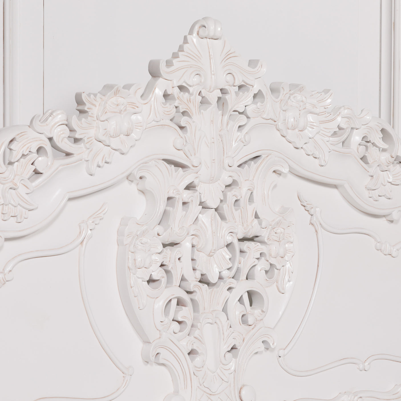 Close-up of an ornate white carved headboard with intricate floral and scrollwork details against a matching white background.