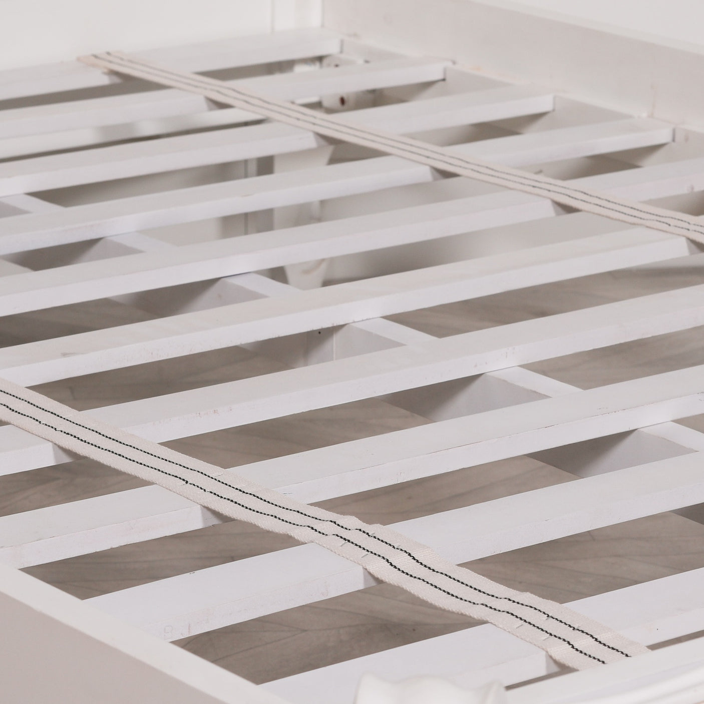 White wooden bed slats with two beige woven mattress support strips, shown close-up on a bed frame.