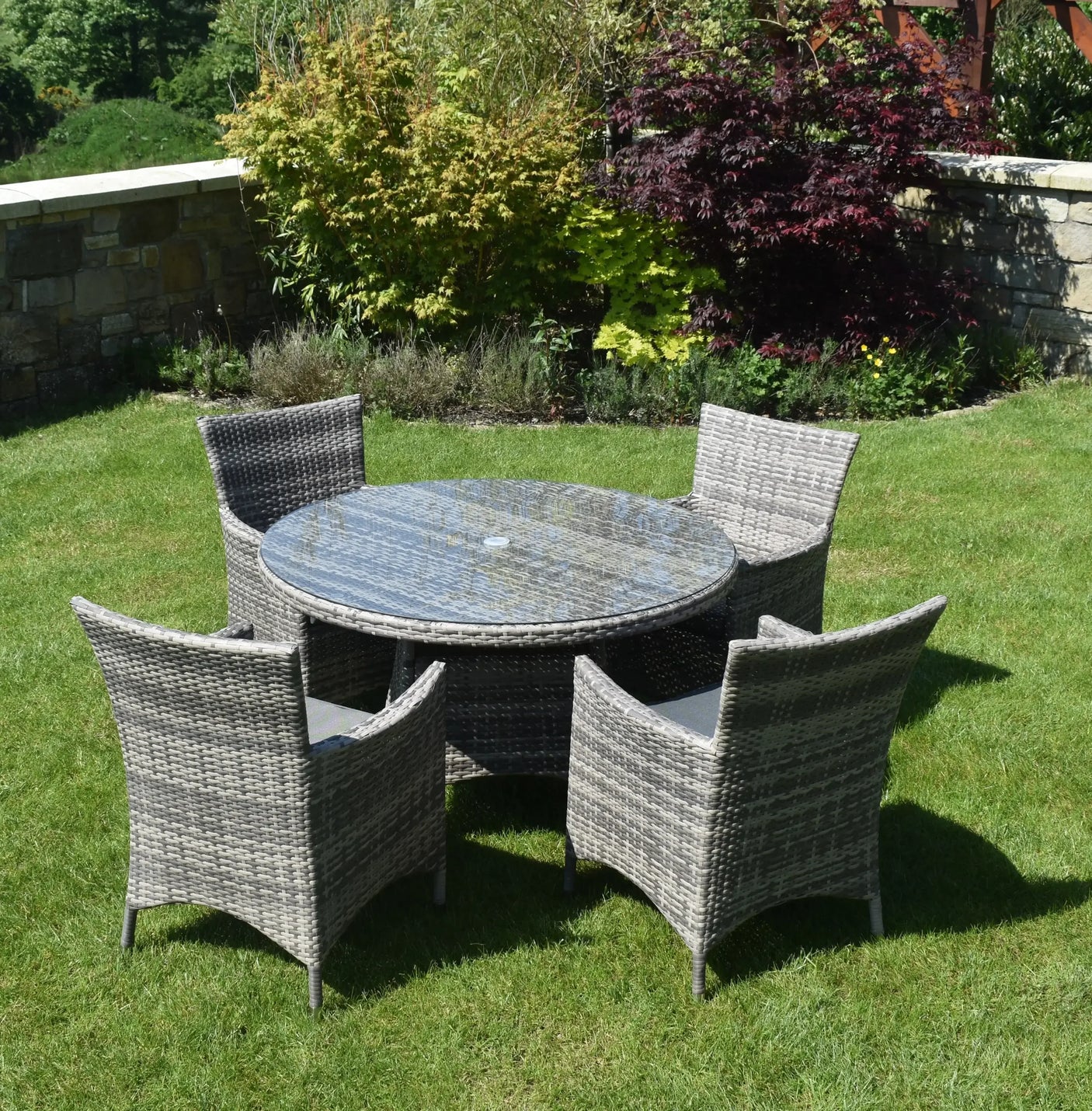 Rattan outdoor dining set with round glass table and four armchairs on garden lawn