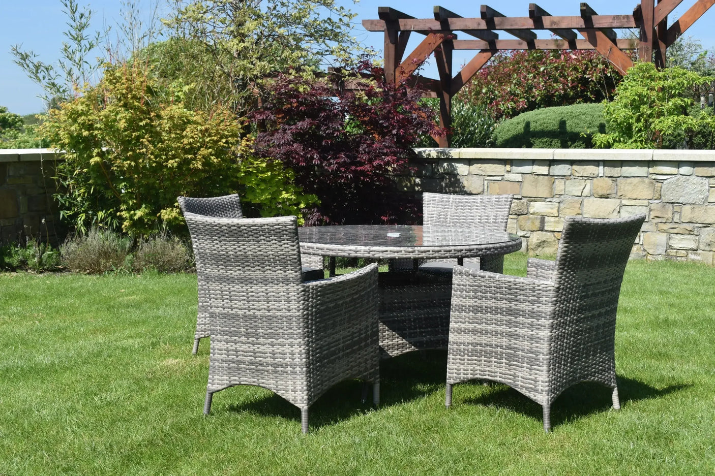 Rattan dining set with round glass table and four chairs on green lawn