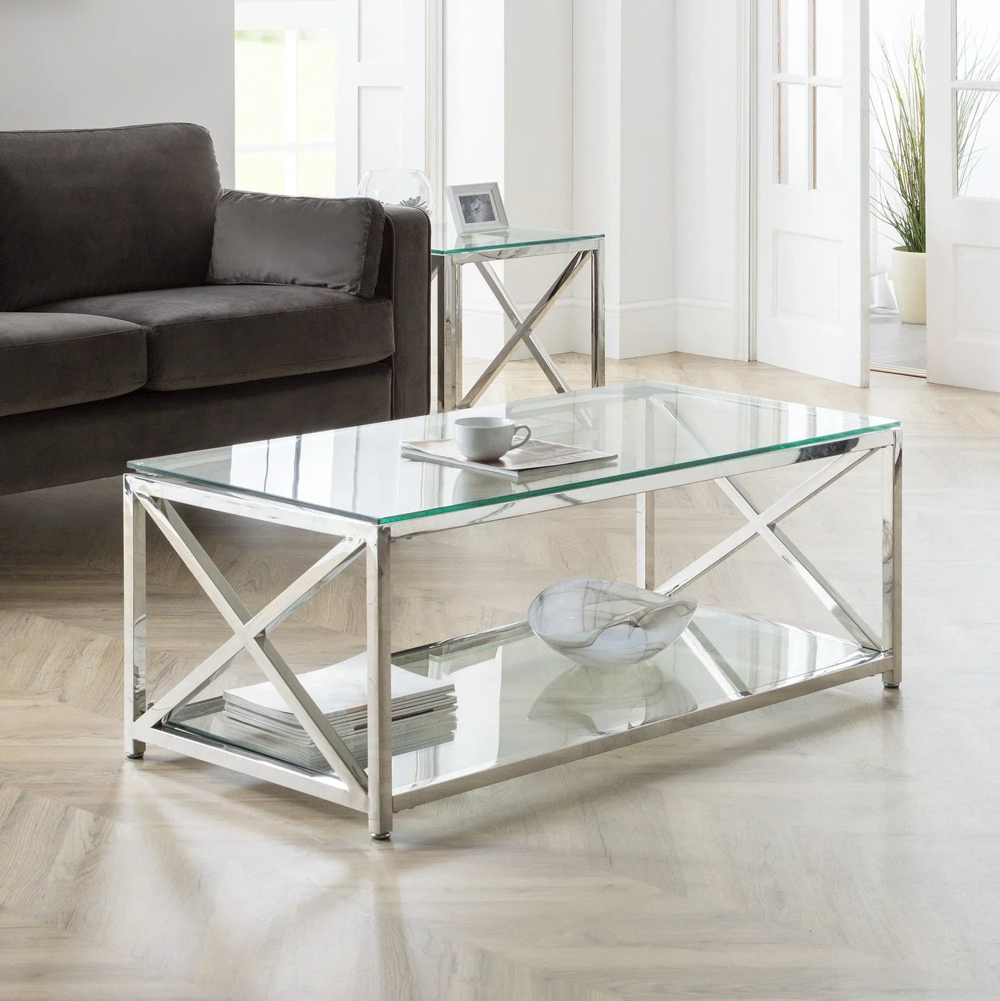 glass coffee table with chrome frame and shelf in modern living room beside grey sofa
