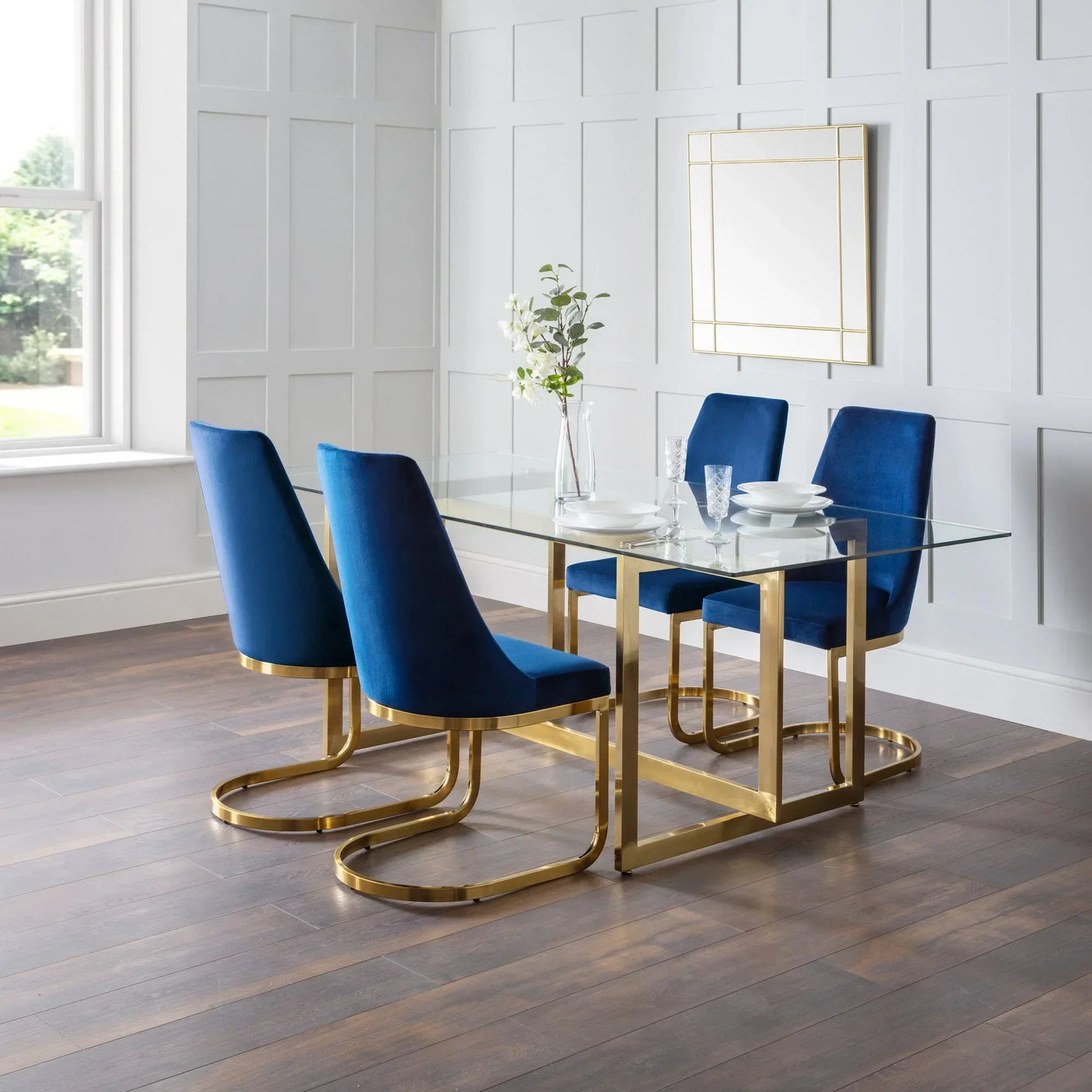 Glass dining table with gold legs and four blue velvet chairs in modern dining room