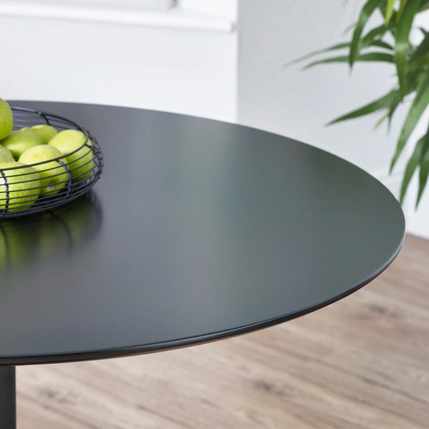 Round black dining table with metal fruit basket, close up on smooth tabletop