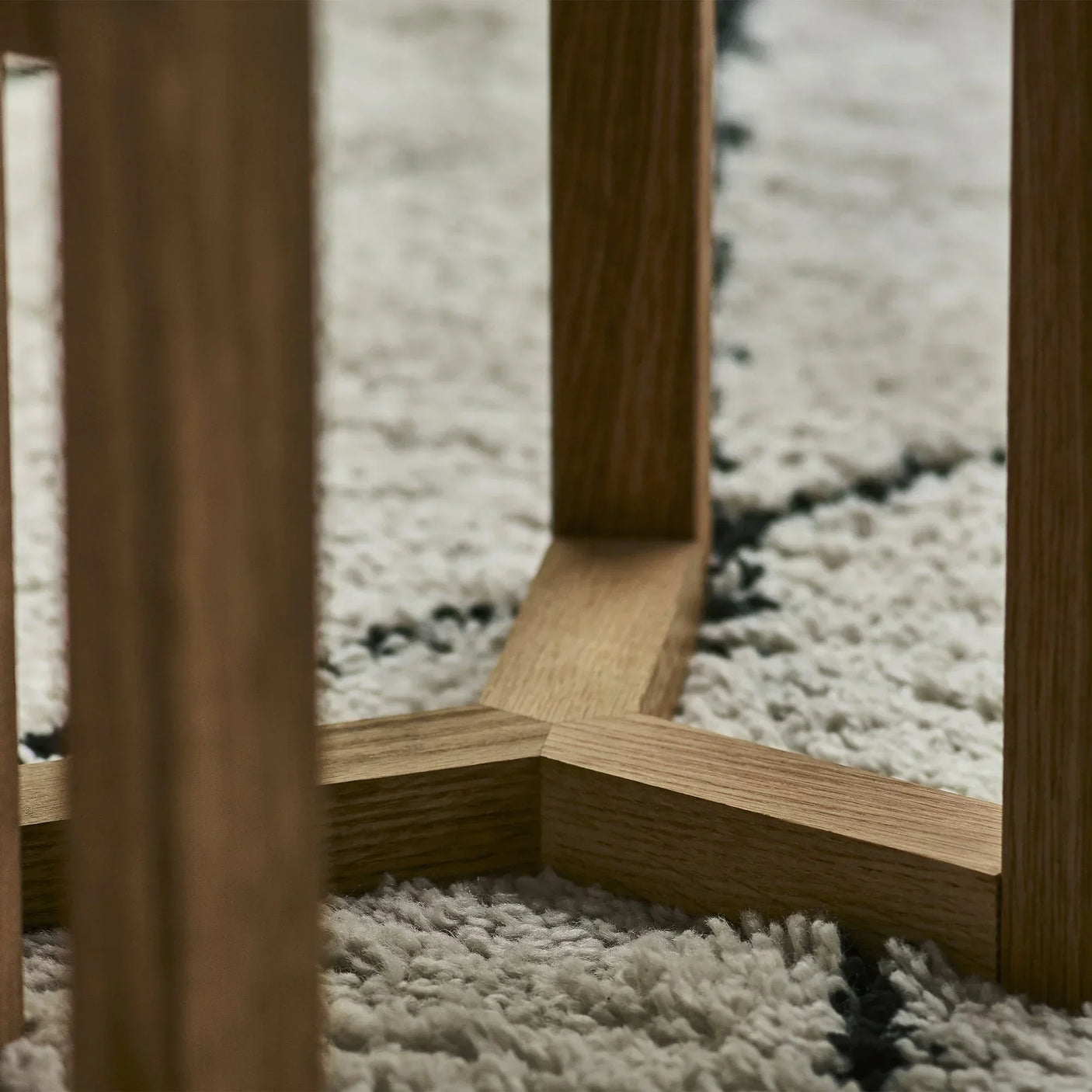 Close-up of wooden nest of tables leg joinery on textured cream and black rug