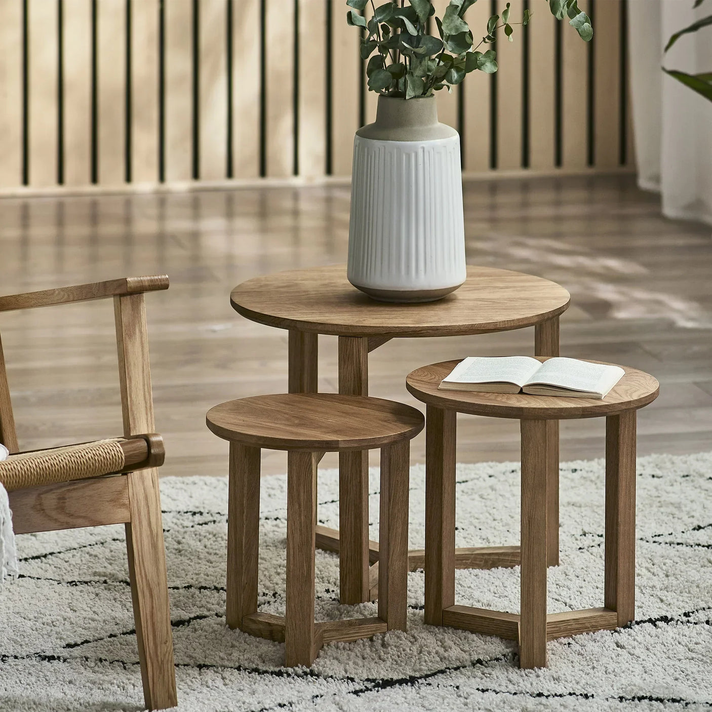 Oak nest of tables set on patterned rug with ceramic vase and open book