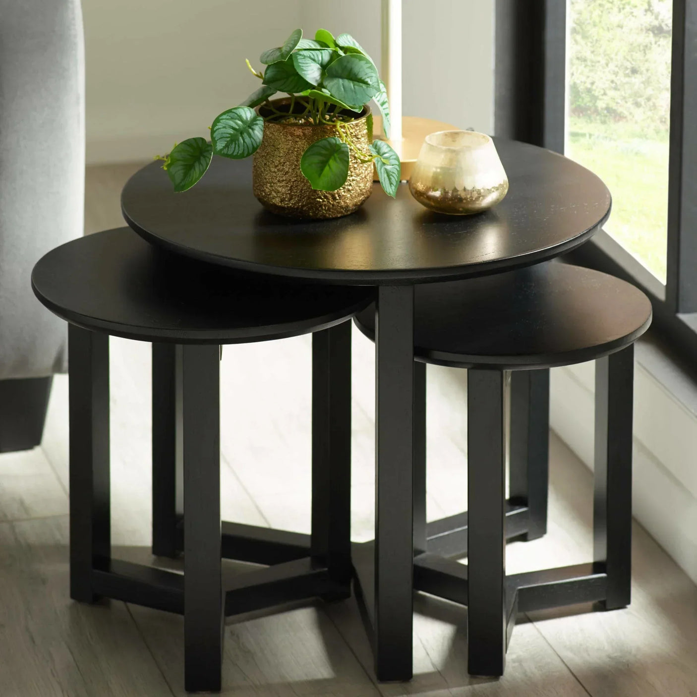 Black wooden nest of tables with gold plant pot and candle in bright living room corner