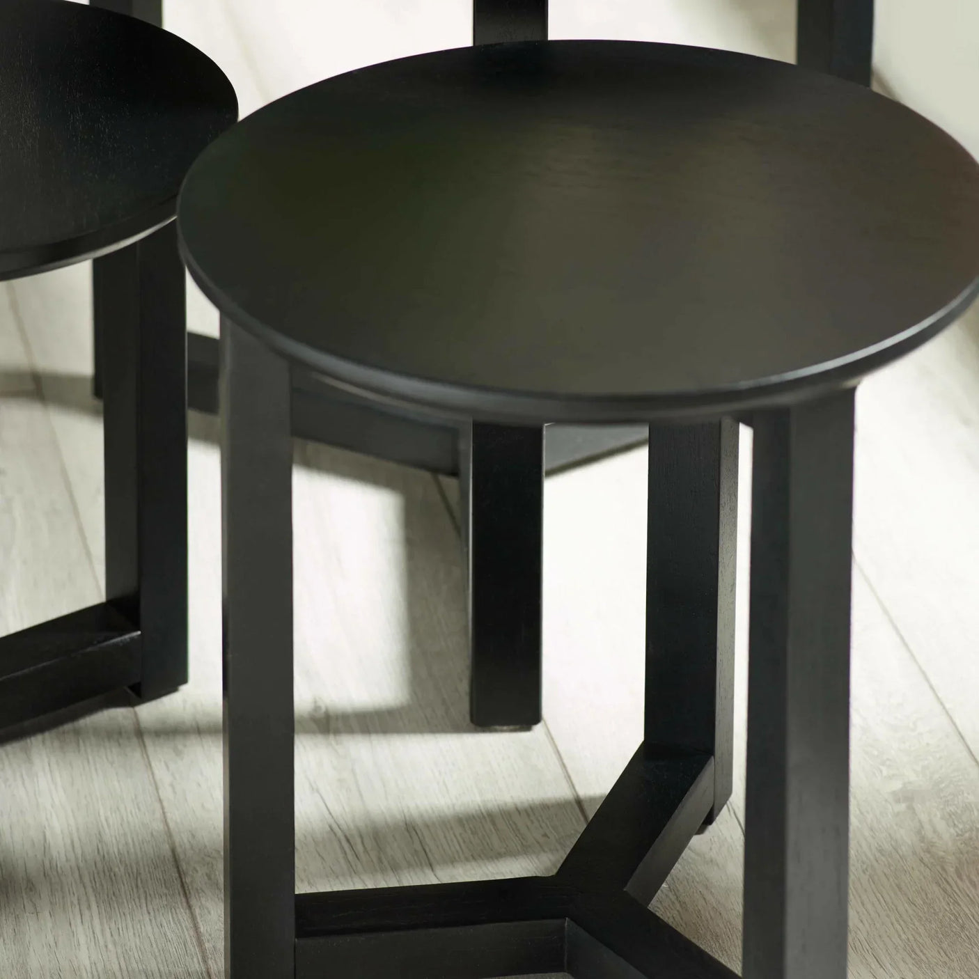 Black round wooden side table set with modern legs on light laminate floor