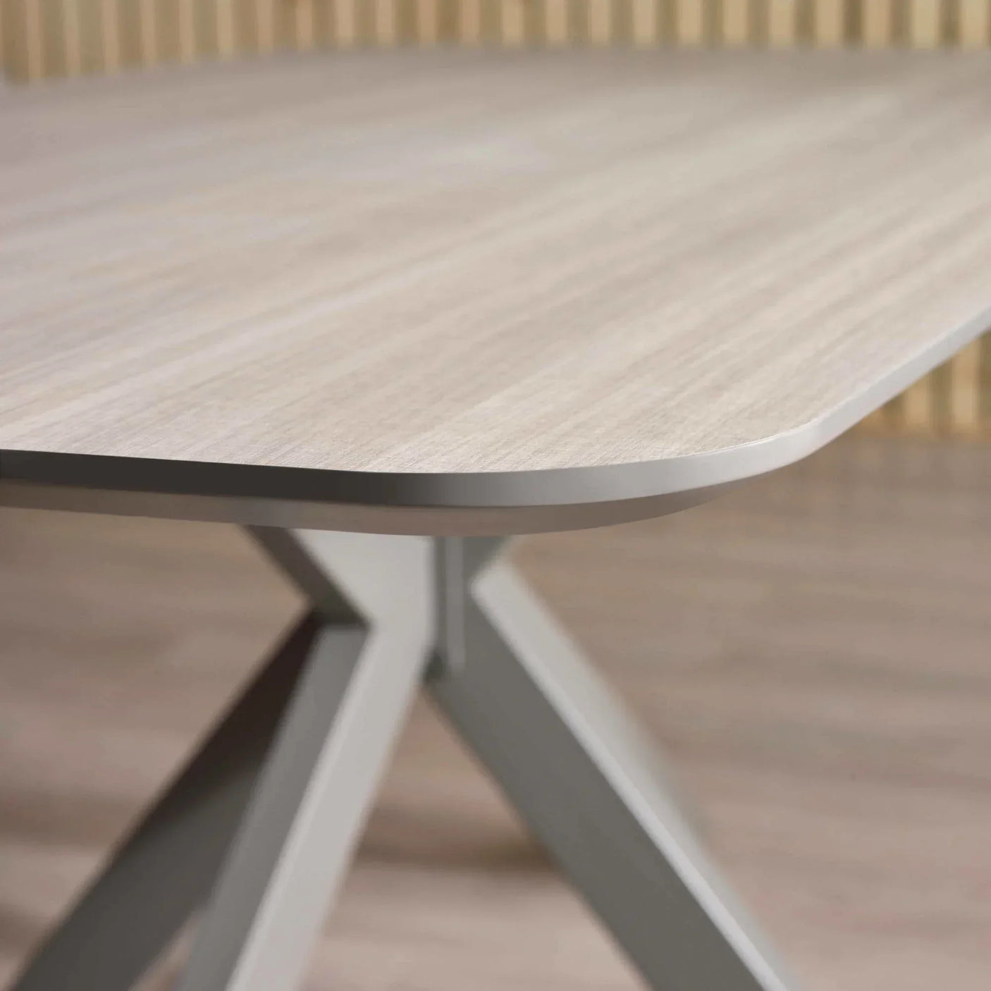 Close view of light oak dining table with angled metal legs and rounded edge detail