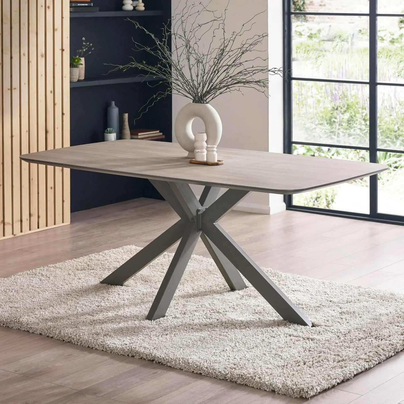 Modern dining table with light wood top and metal legs on a textured rug in dining room