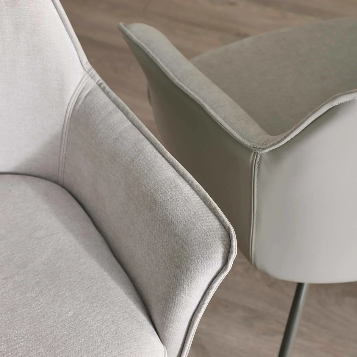 Light grey fabric dining chairs with curved arms on wooden flooring