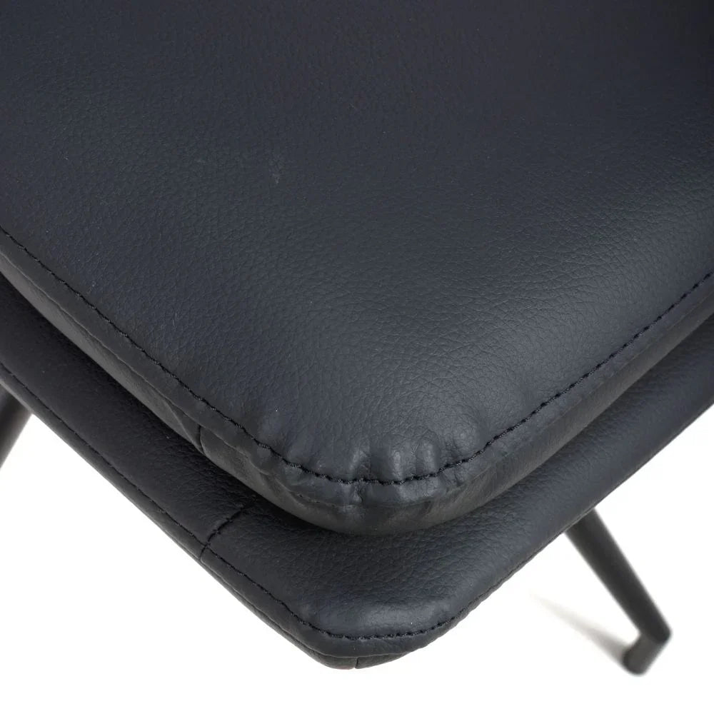 Closeup of black faux leather dining chair seat with stitched edge and metal legs
