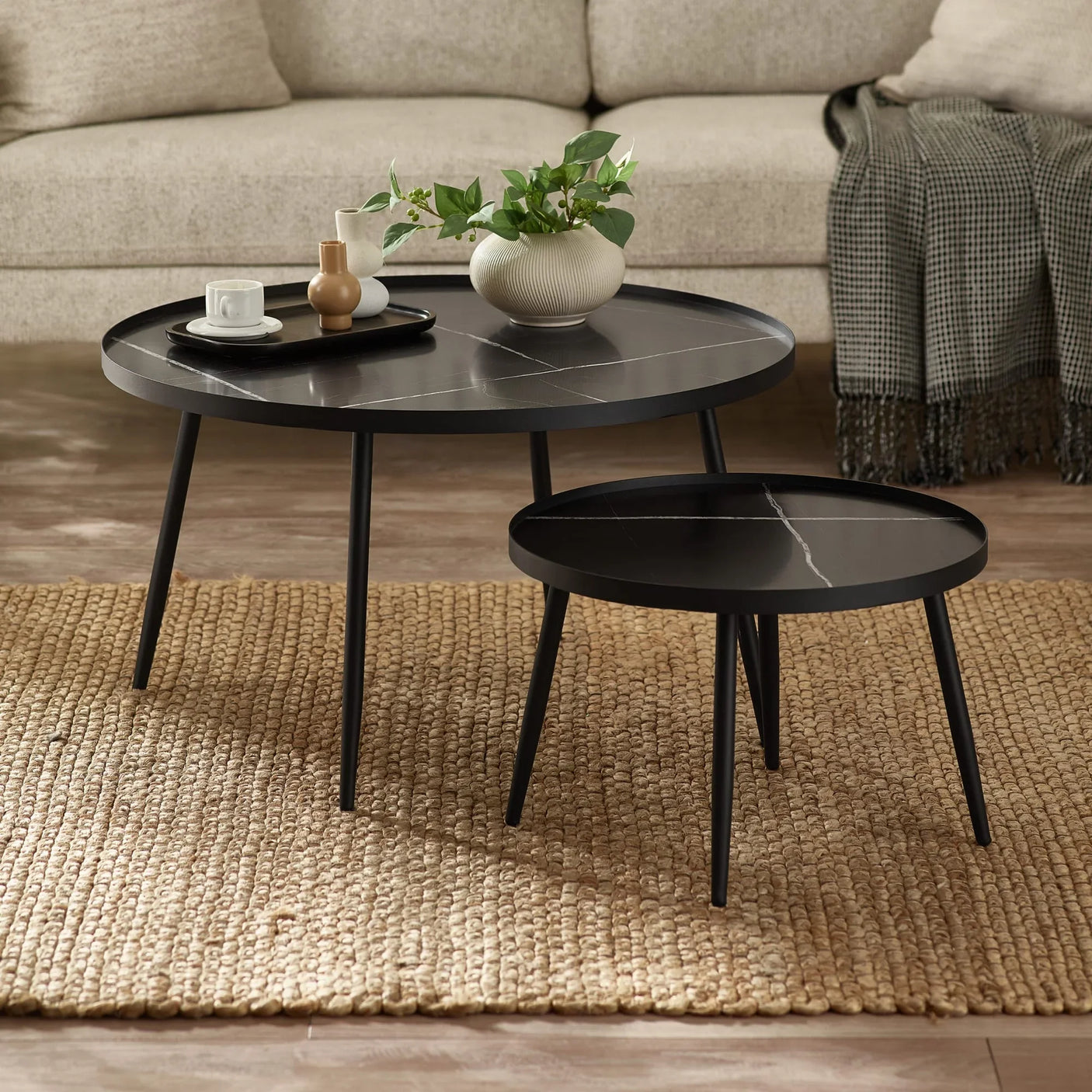 Black nesting coffee tables with vases and cups on natural woven rug in living room