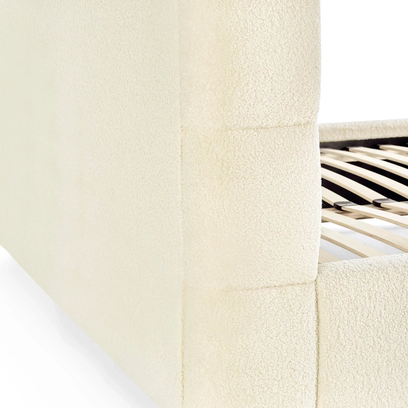 Closeup of cream fabric bed frame corner with slatted wooden bed base