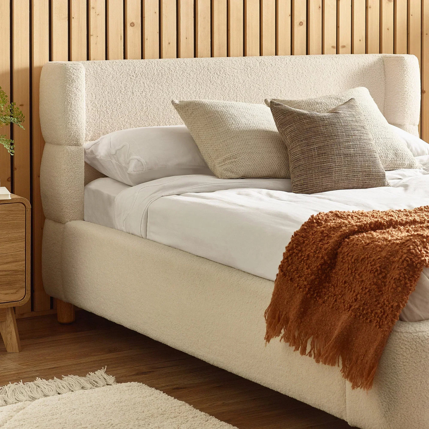 Cream upholstered bed frame with textured headboard, white bedding and rust throw blanket