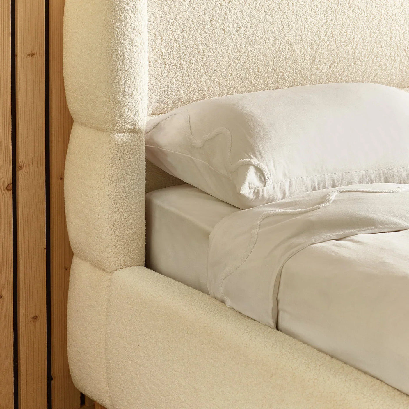 Closeup of cream boucle upholstered bed frame and headboard with white bedding