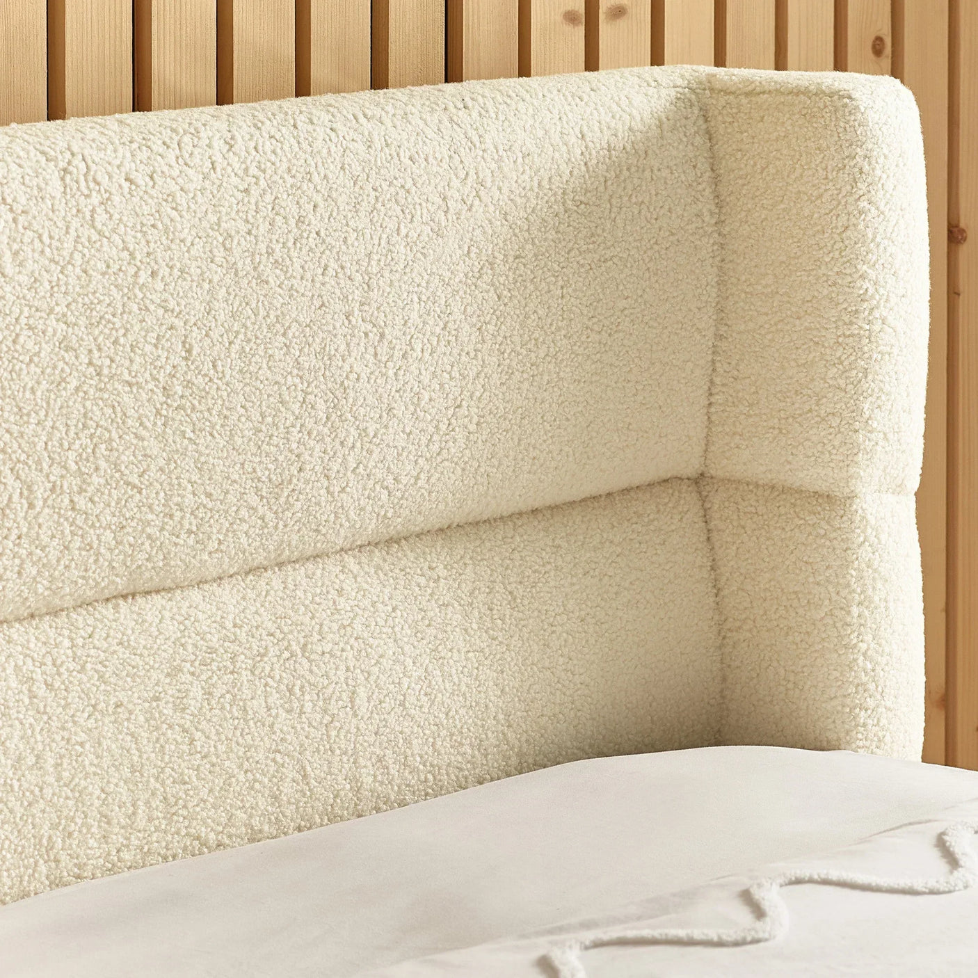 Cream boucle upholstered bed headboard with vertical panel design against wood slat wall