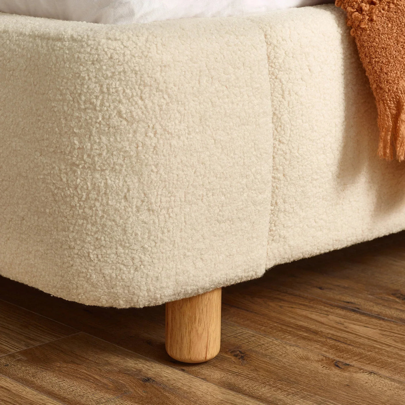 Cream boucle bed frame corner with wooden leg on wooden floor