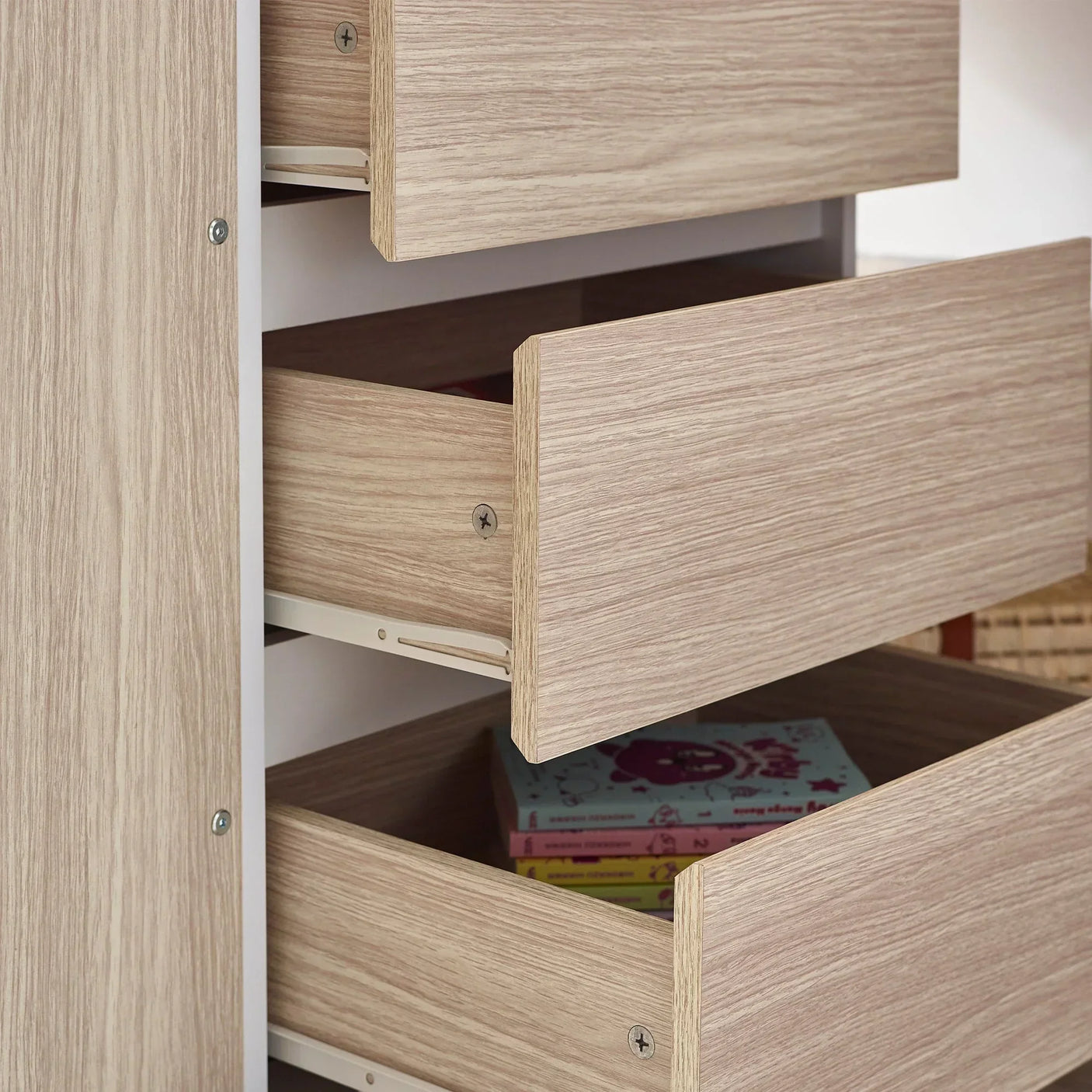 Pale wood chest of drawers with two open drawers, books visible inside lower drawer