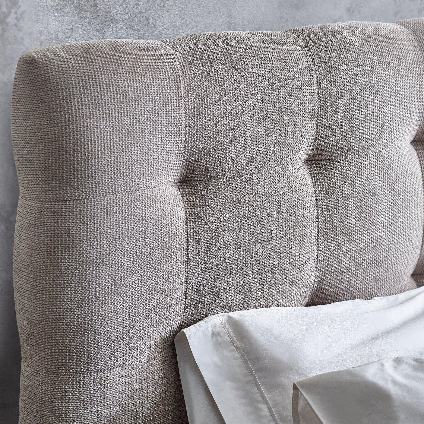 Light grey upholstered bed headboard with textured fabric and vertical tufting detail