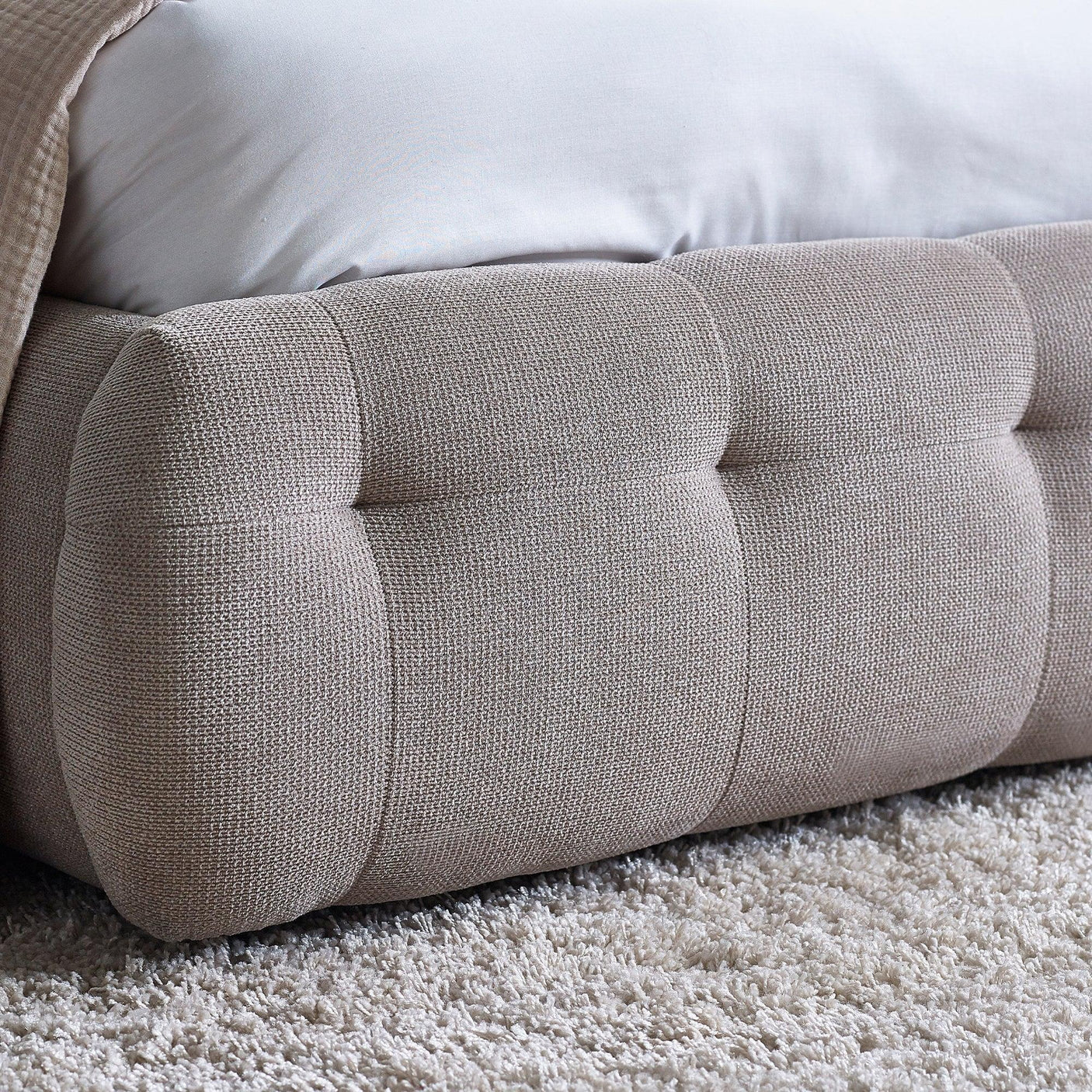 Beige upholstered bed frame with textured fabric detail and low profile foot end