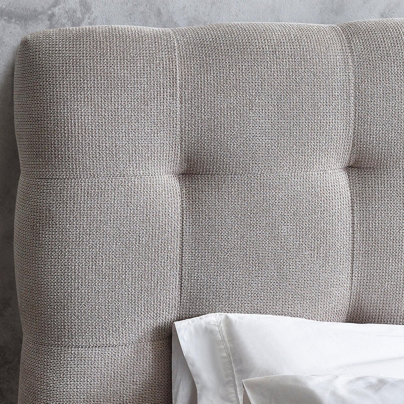 Light grey fabric bed headboard with tufted detail and white pillow visible