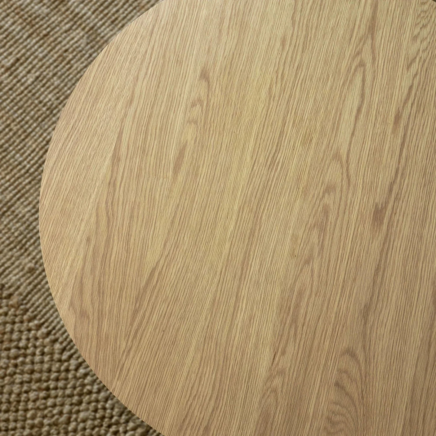 Close view of round oak dining table top on textured beige rug