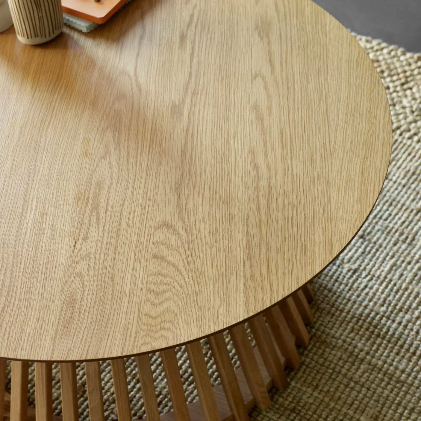 Round oak coffee table with slatted wooden base on beige textured rug