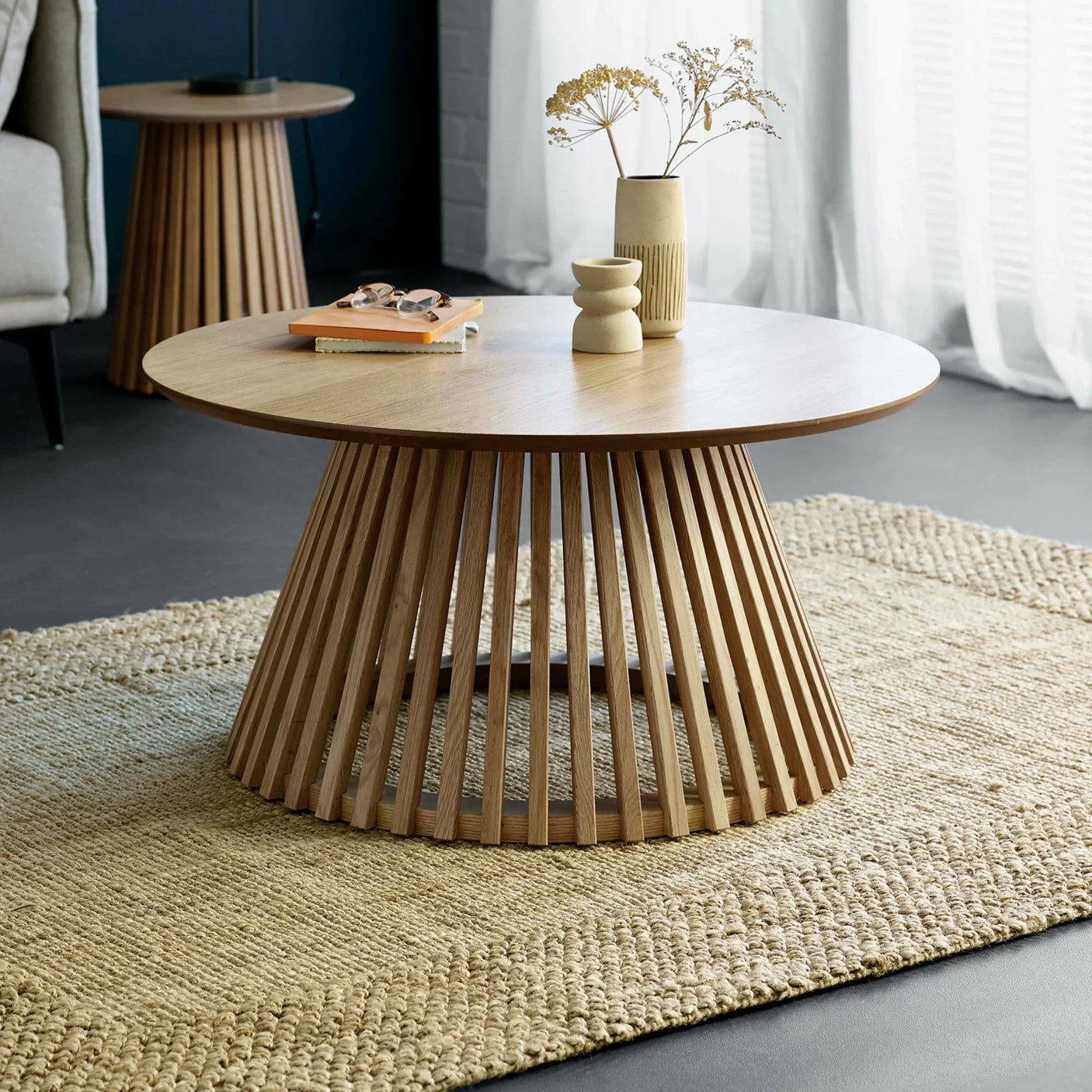 Round wooden coffee table with slatted base on woven rug in living room