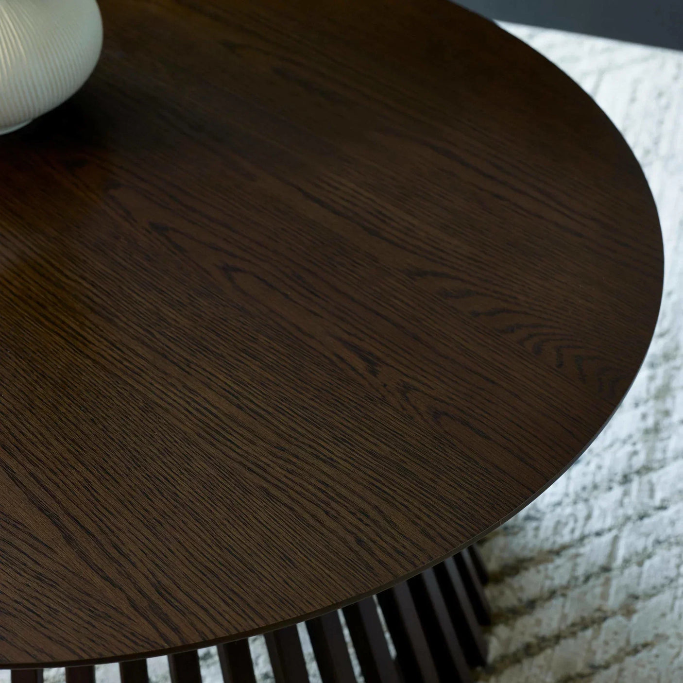 Round dark wood dining table top with visible grain, modern black base, textured rug below
