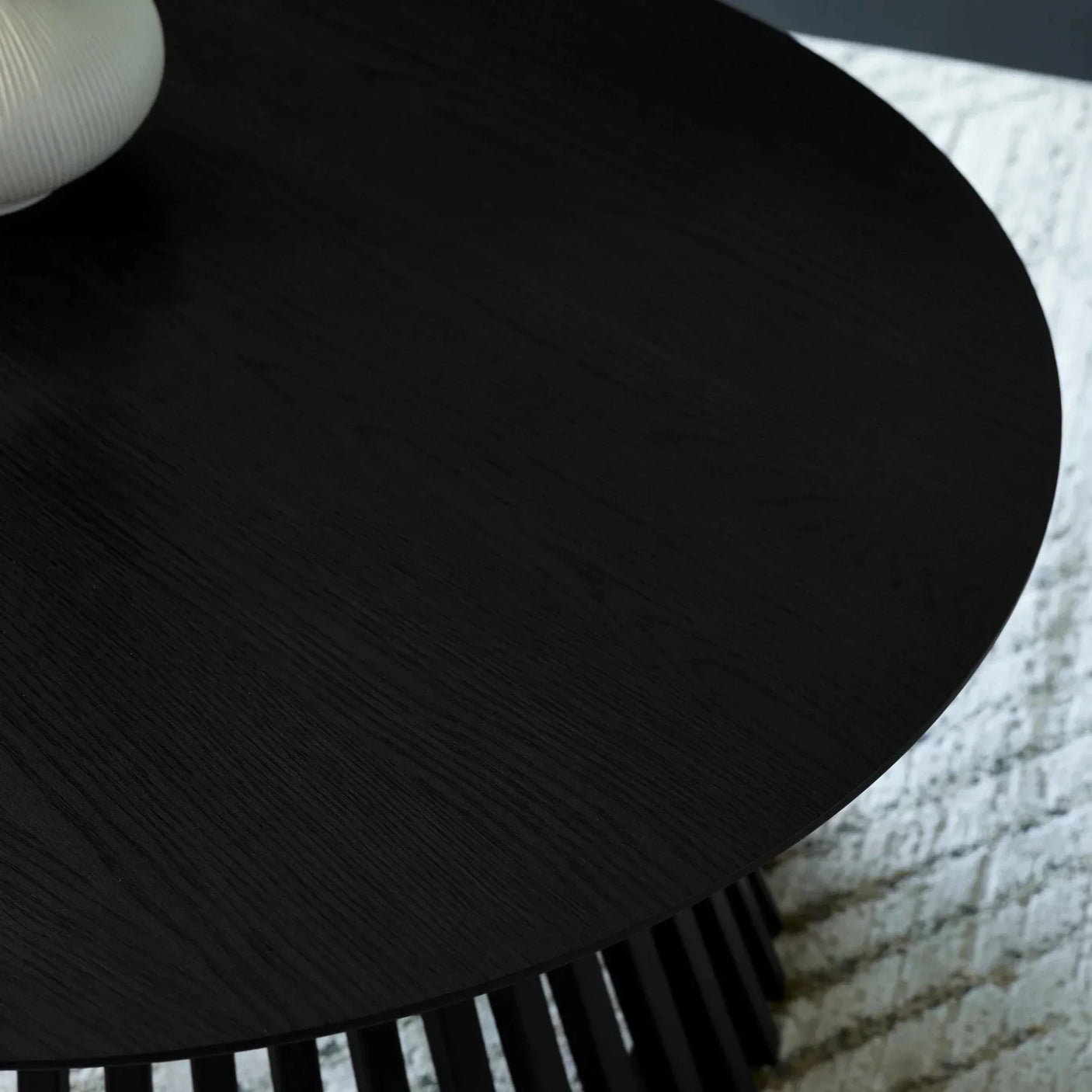 Round black wood coffee table top with textured surface on patterned rug
