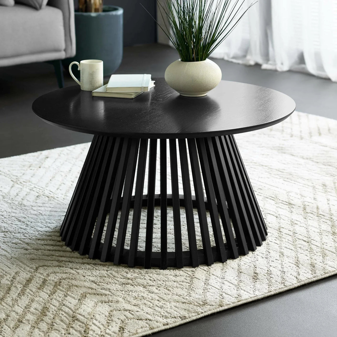 Black round coffee table with slatted base on textured cream rug in modern living room