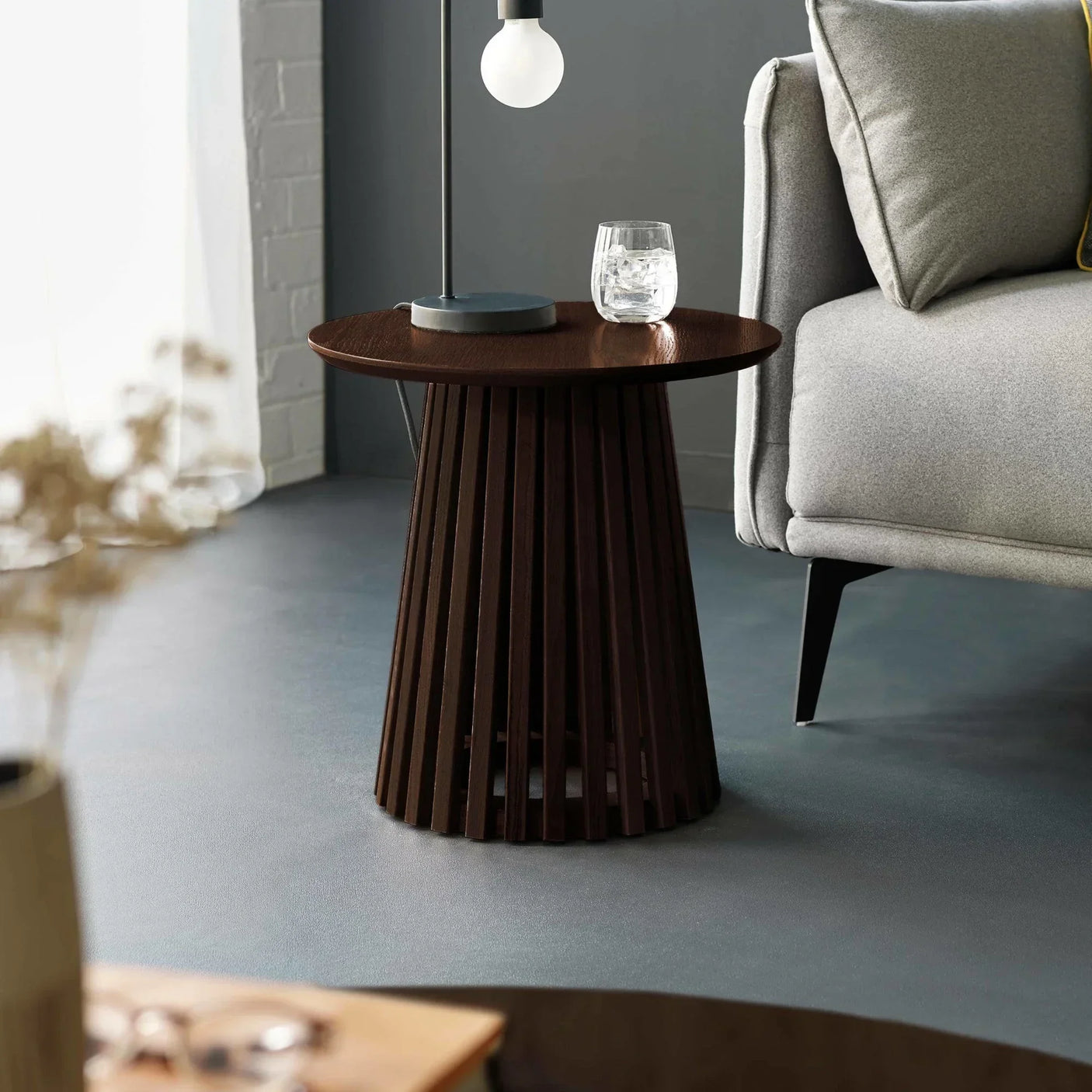 Dark wood slatted side table beside grey sofa, styled with lamp and glass of water
