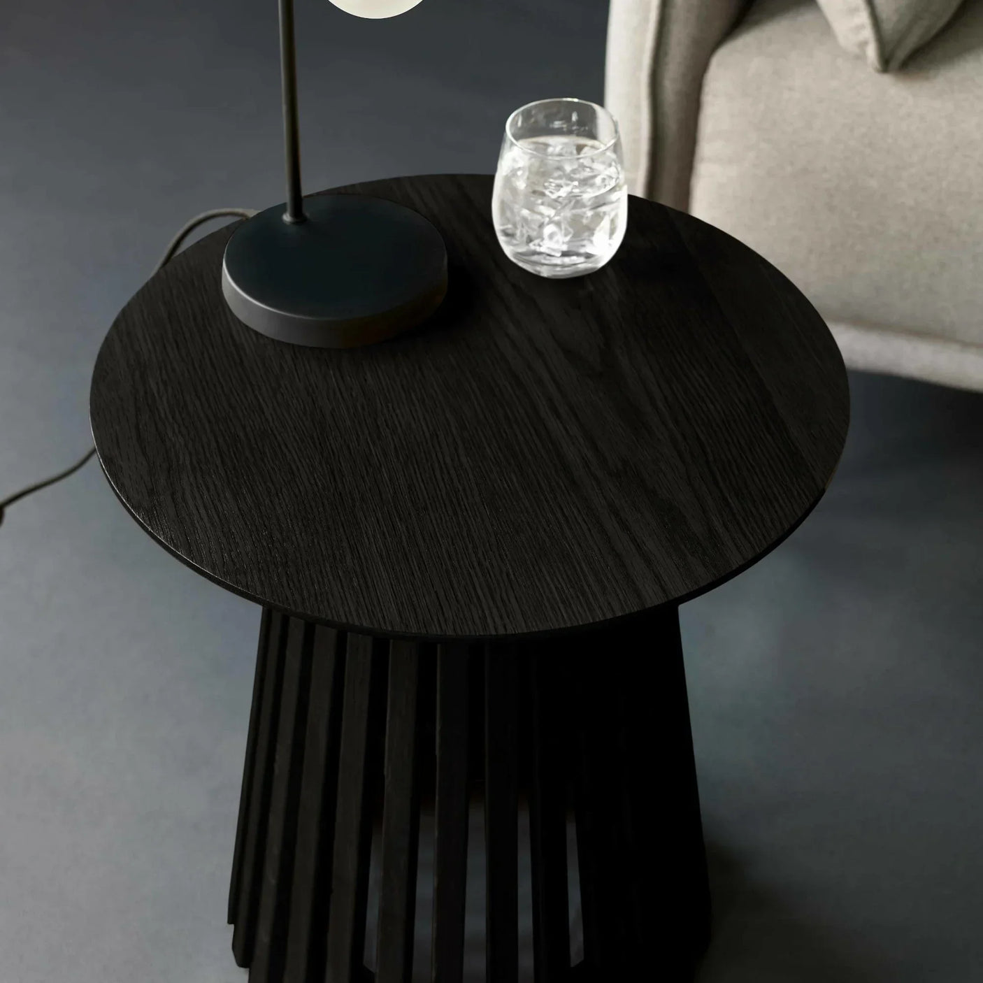 Black wooden side table with modern lamp and glass of water beside sofa