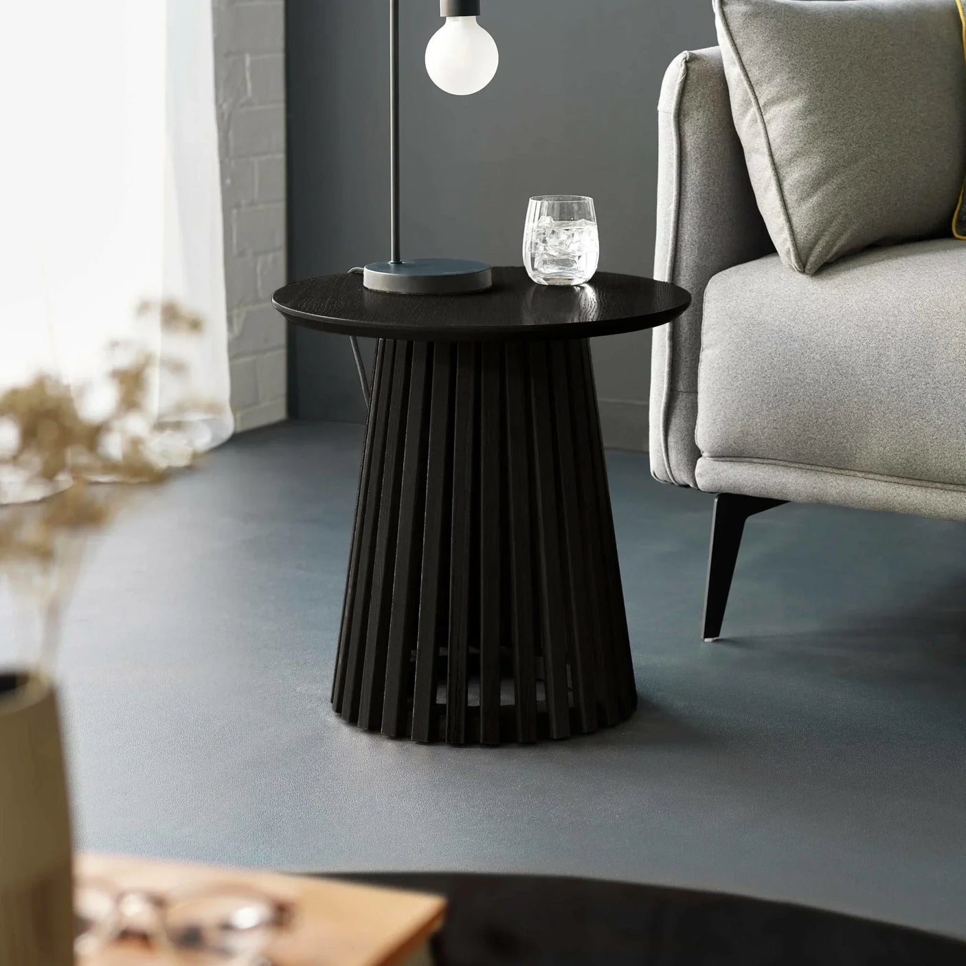 Black wooden side table with slatted base beside grey sofa in modern living room
