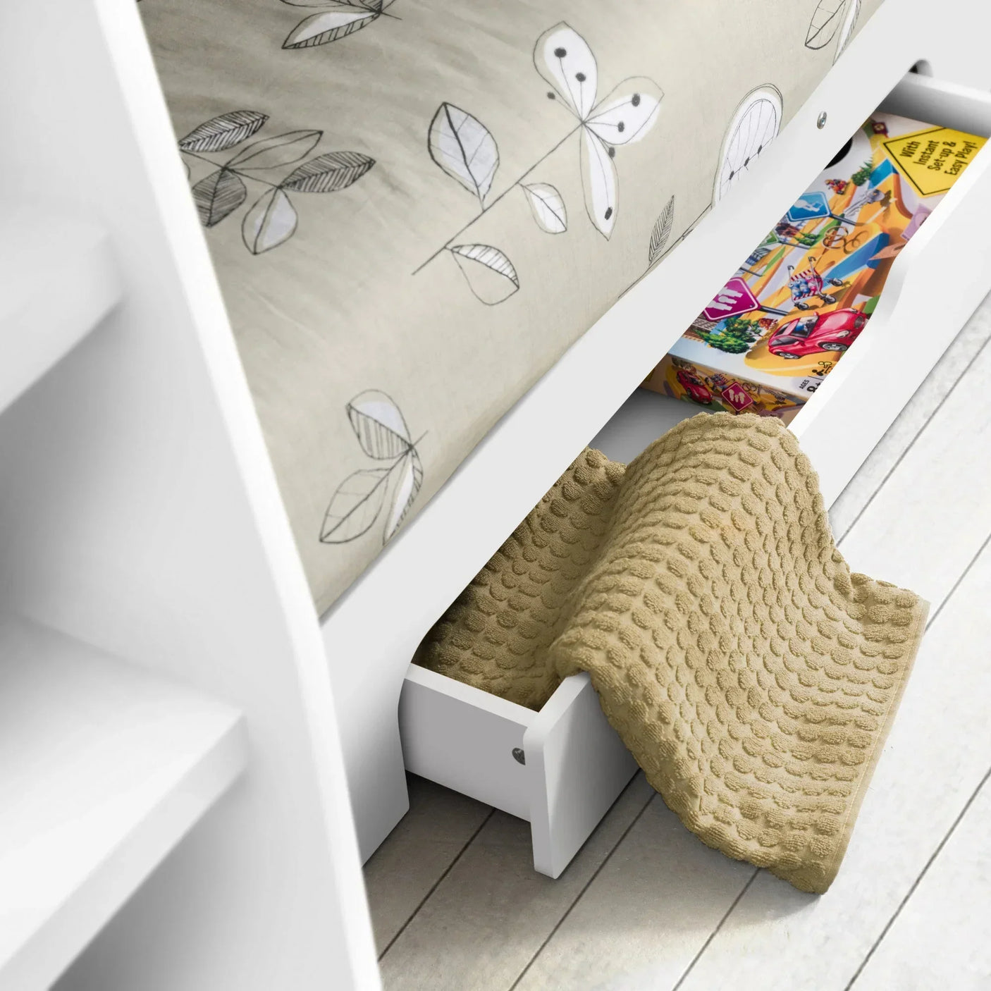 White wooden bed with underbed storage drawer holding a blanket and board game