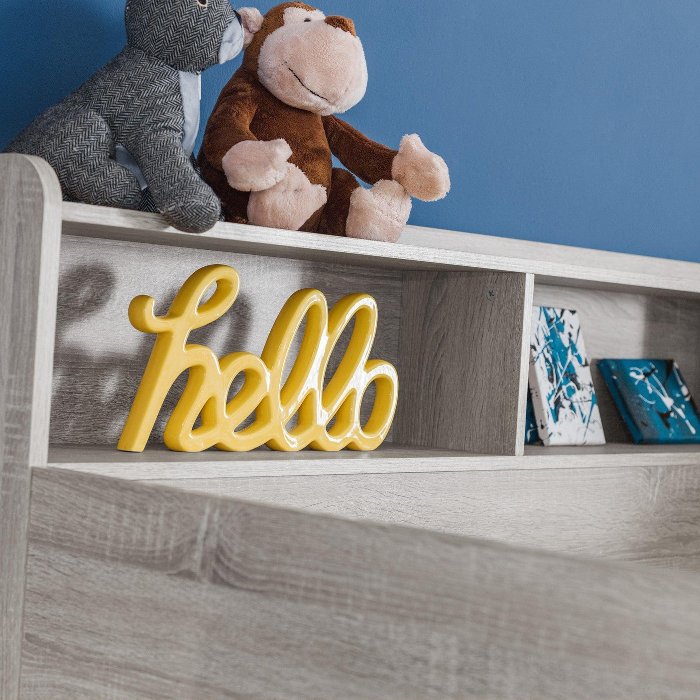 Light wood headboard shelf with plush toys, yellow hello sign, and blue accent wall