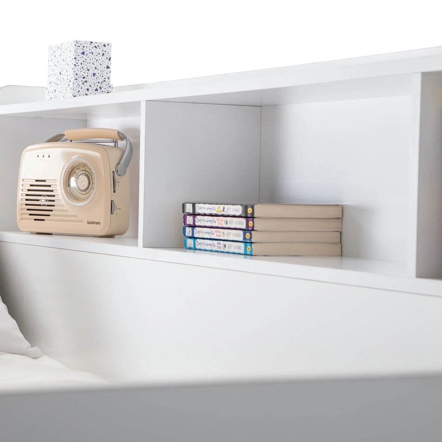 White wooden headboard shelf with books, a beige radio, and a tissue box