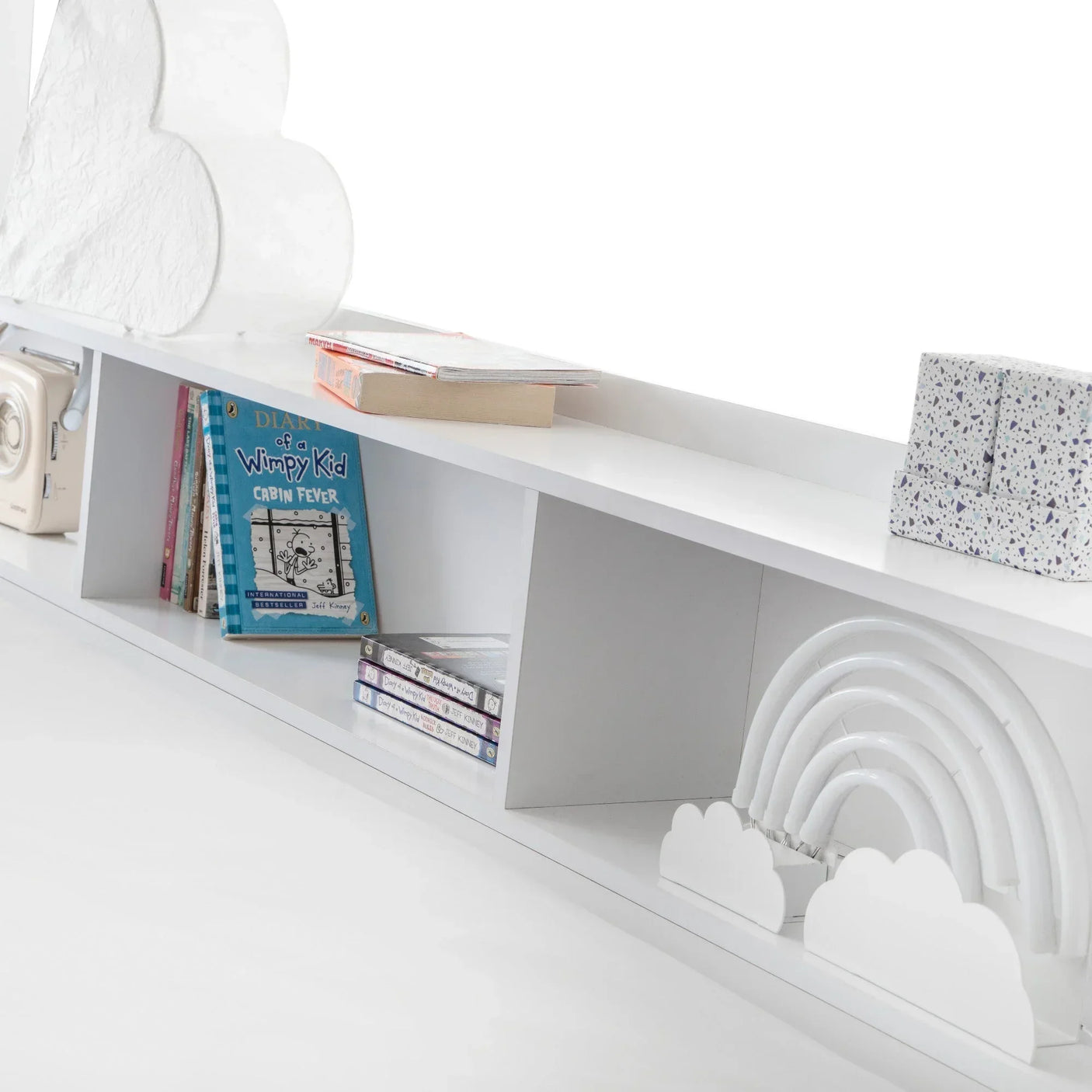 White wooden bookcase shelf with books, cloud decor, rainbow ornament, and storage compartments