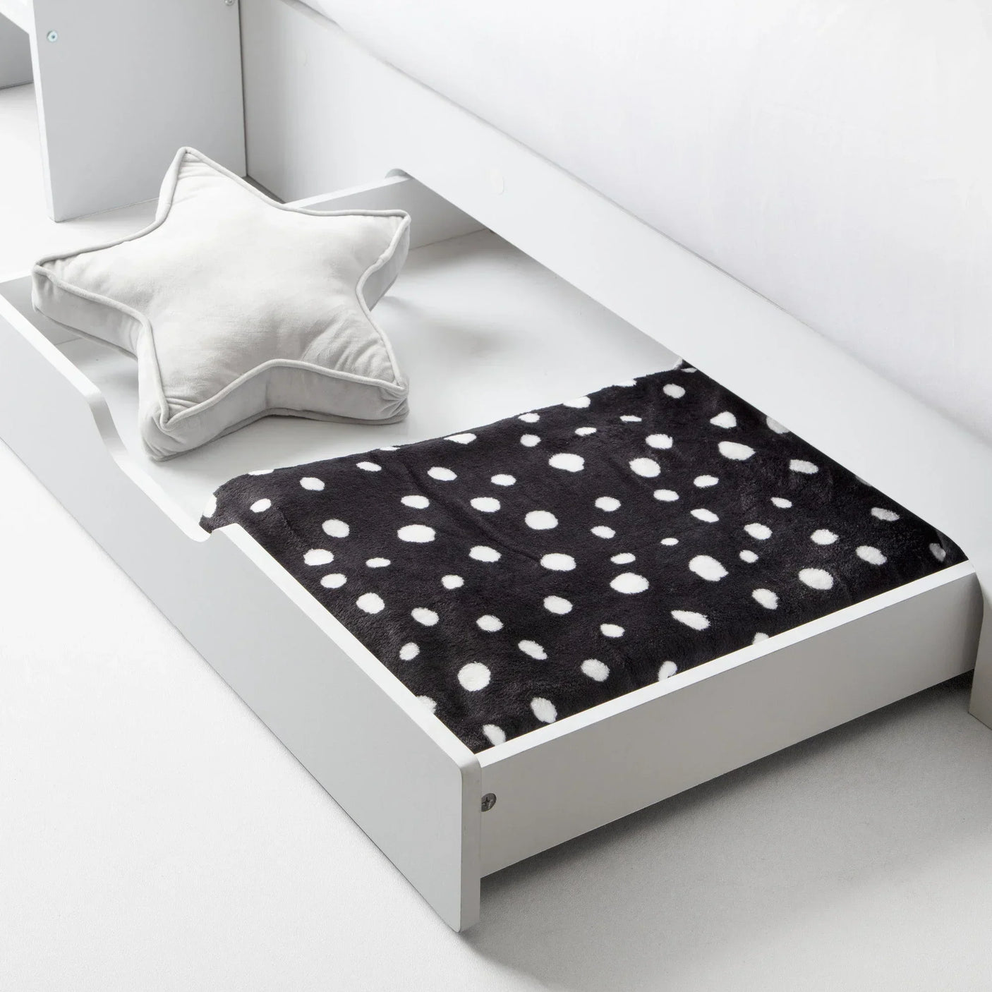 White underbed drawer with black spotted blanket and grey star cushion on light floor