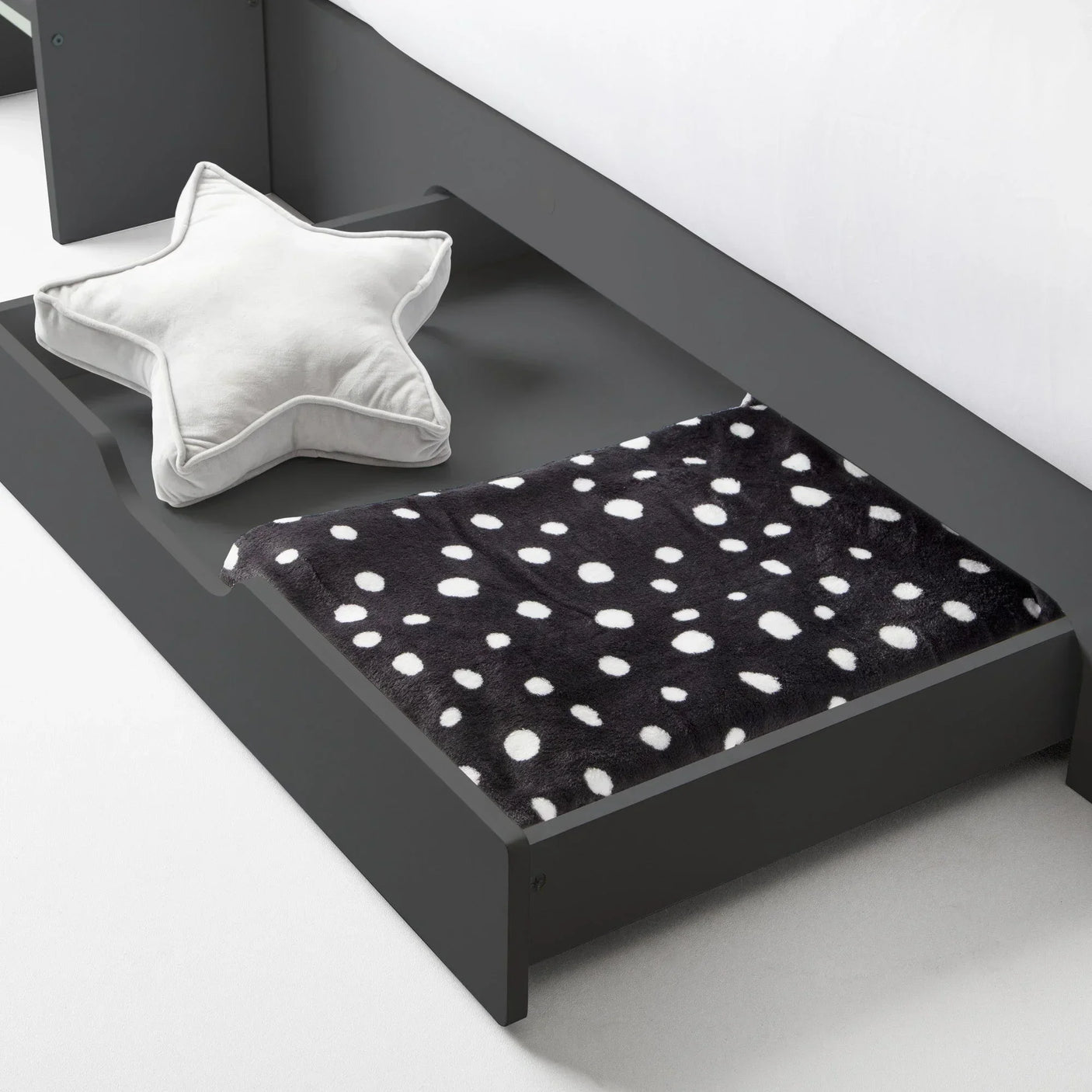 Underbed storage drawer in dark wood with star cushion and black polka dot blanket