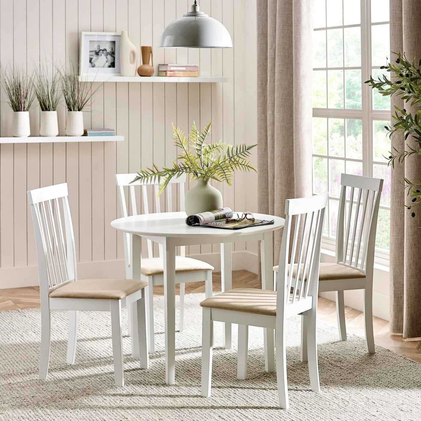 White dining table and four chairs with beige seats in bright dining room with large window