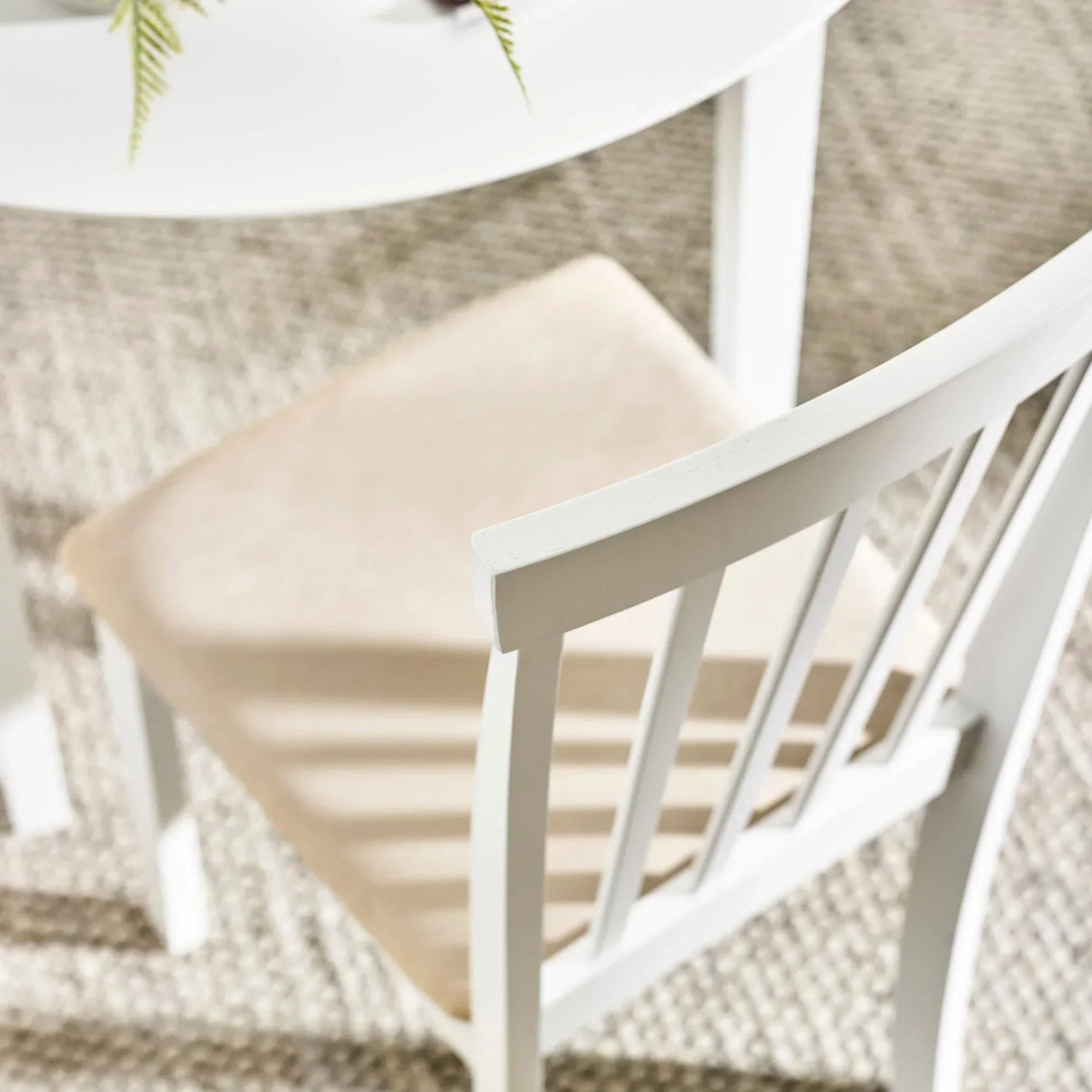 White wooden dining chair with slatted backrest and cushioned seat next to round table