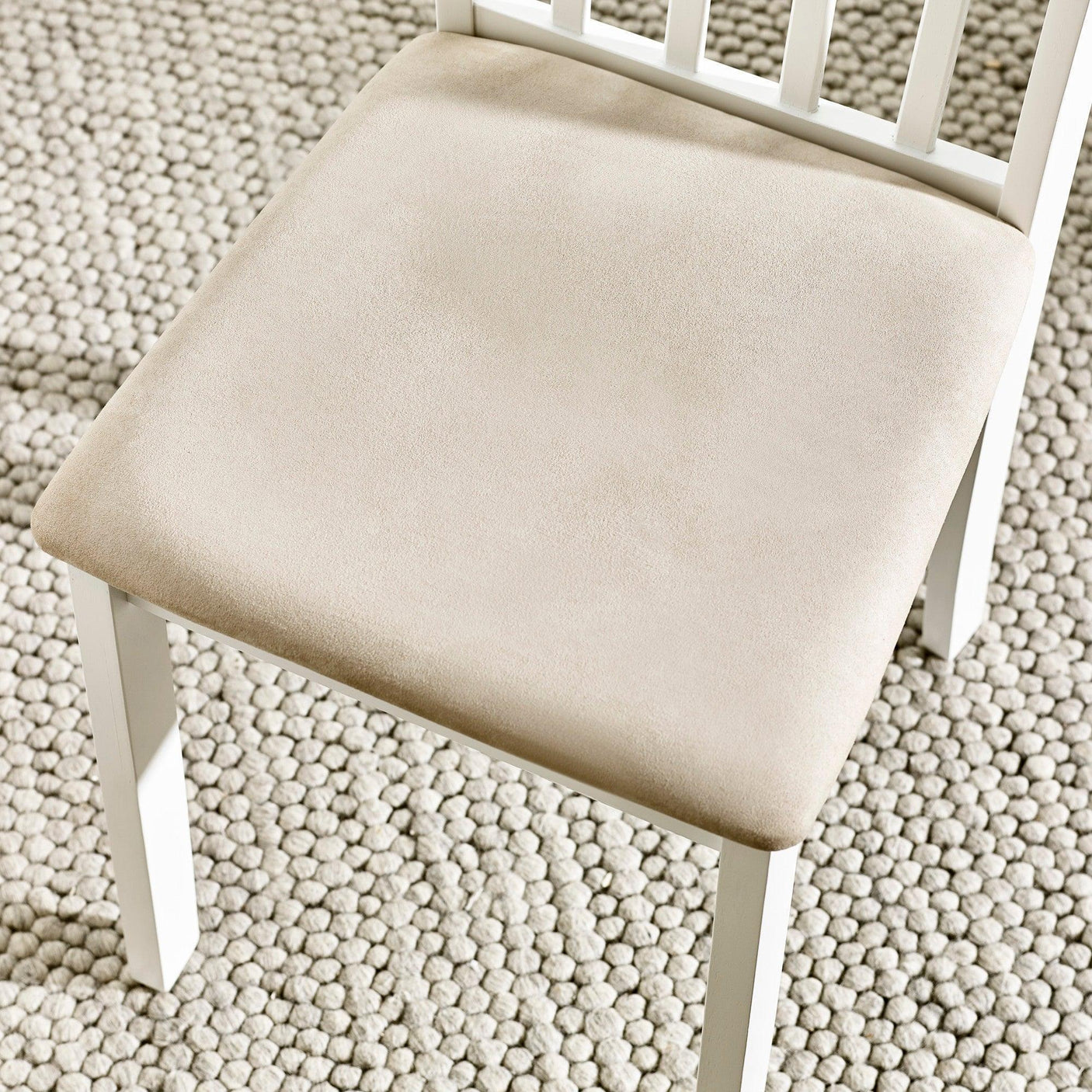 Beige upholstered dining chair seat with white wooden frame on textured rug