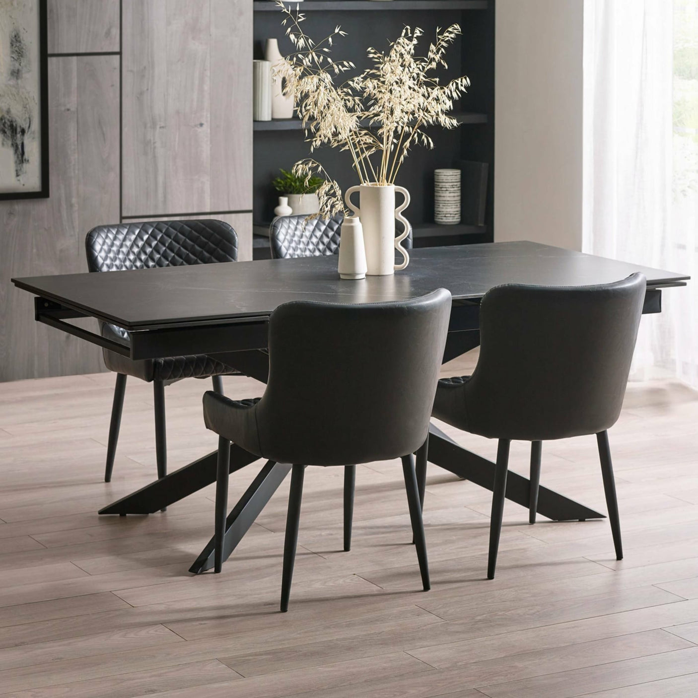 Matte black extending dining table with four black quilted leather chairs in modern indoor setting