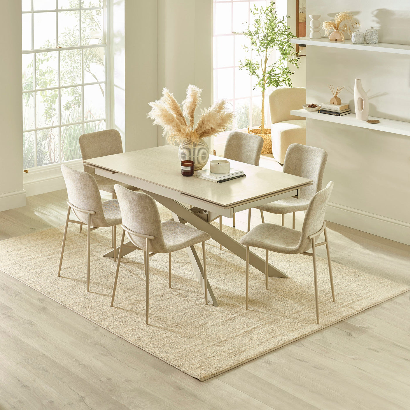 Light beige dining table with six chairs in bright dining room with large windows and decorative vase