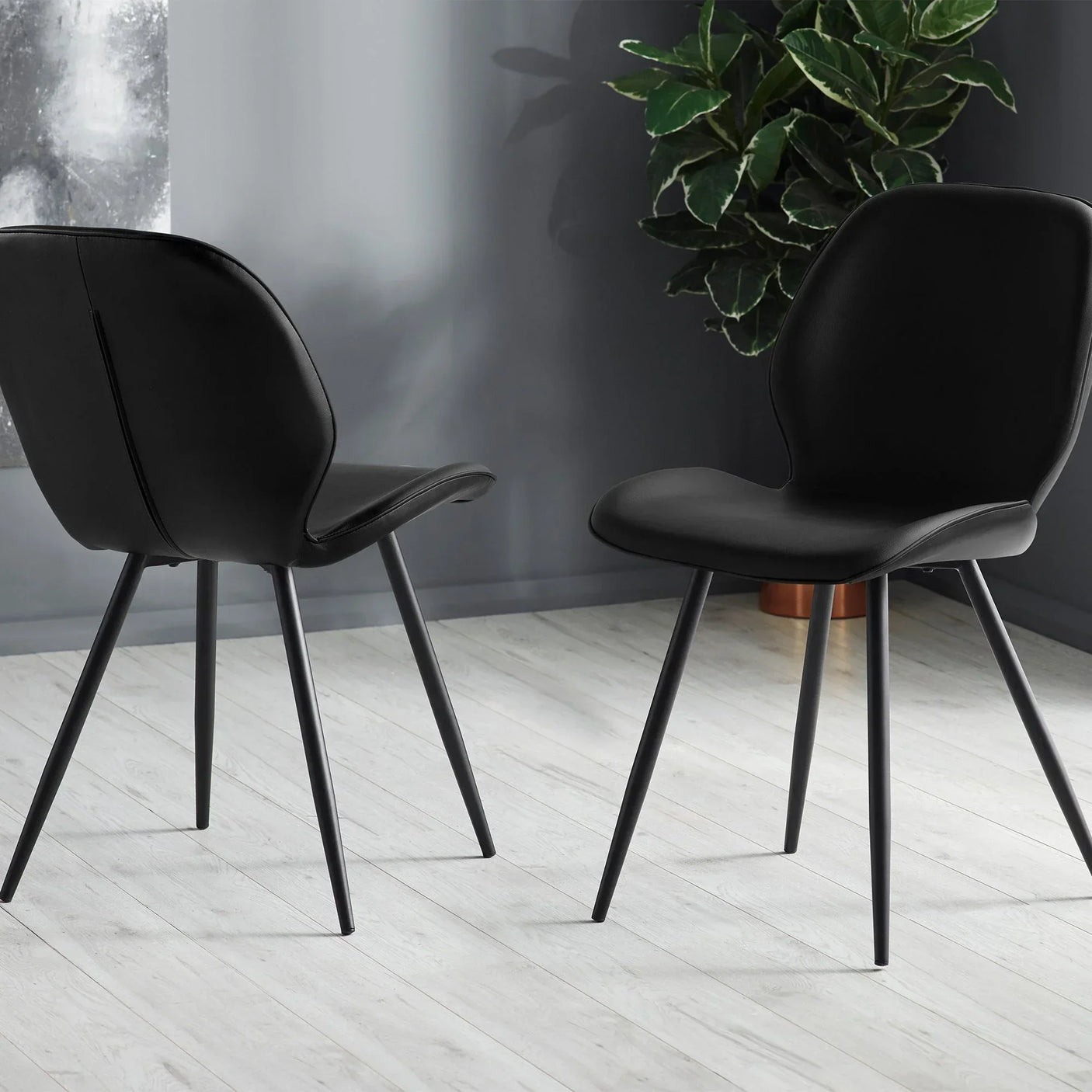 Black dining chairs with slim metal legs on light wood floor in modern room