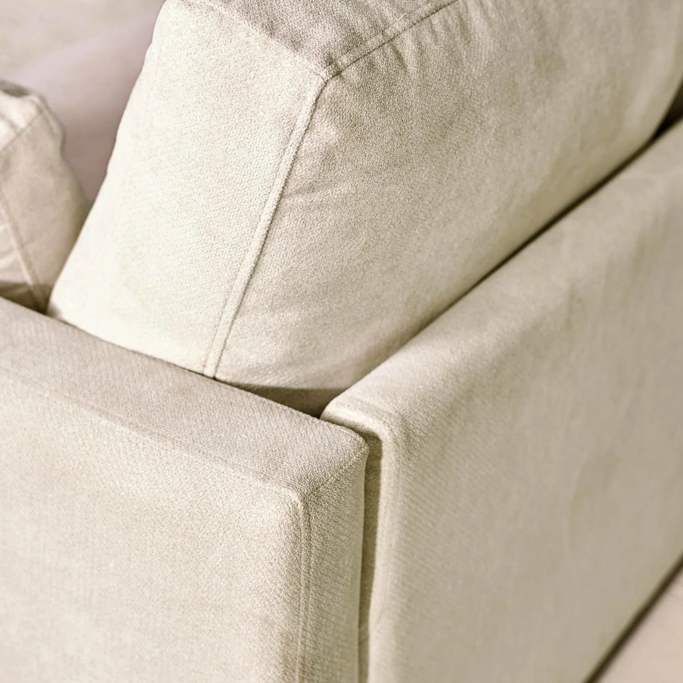 Closeup of beige fabric sofa corner with plush back and seat cushions