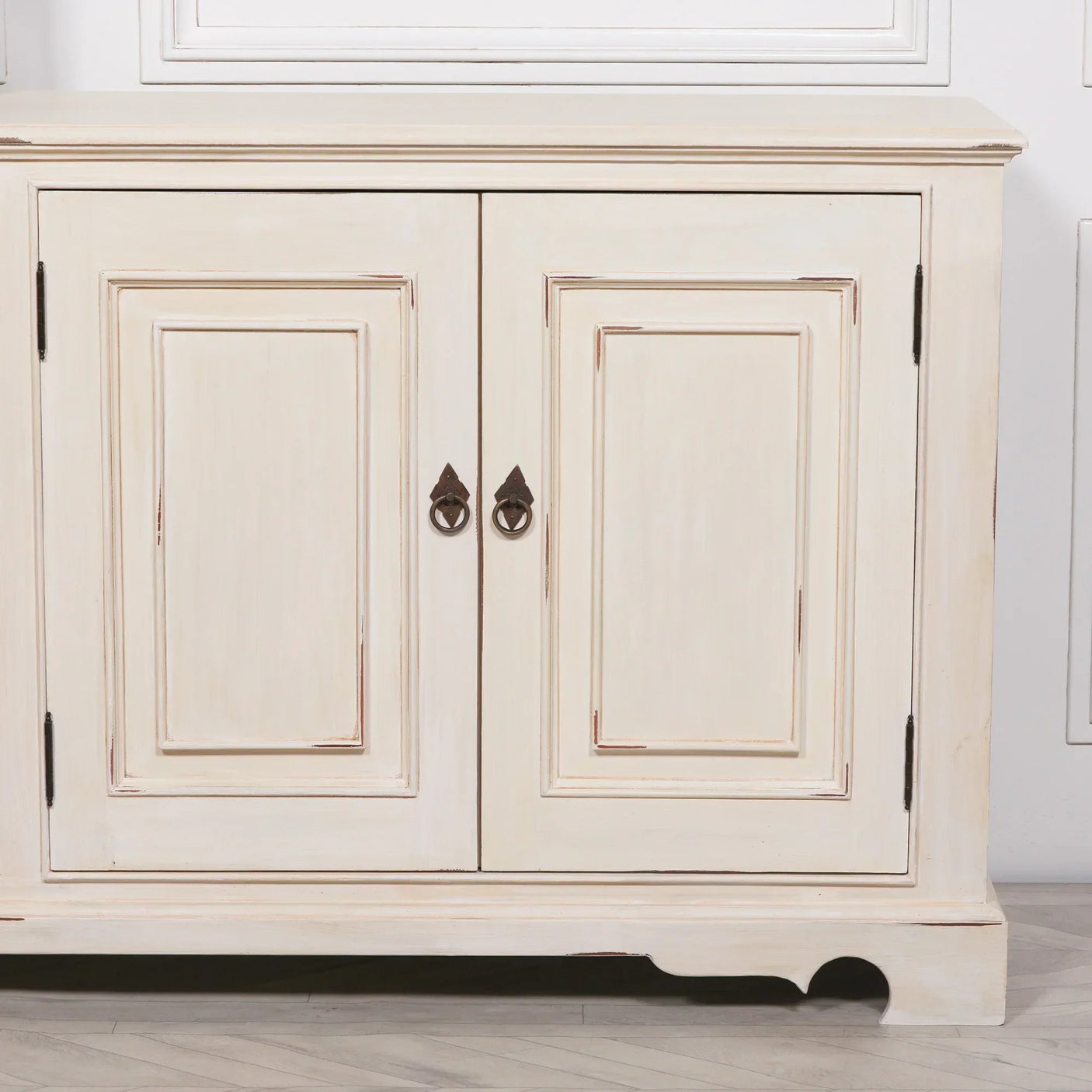 Cream wooden sideboard with two paneled doors and metal ring handles on light flooring