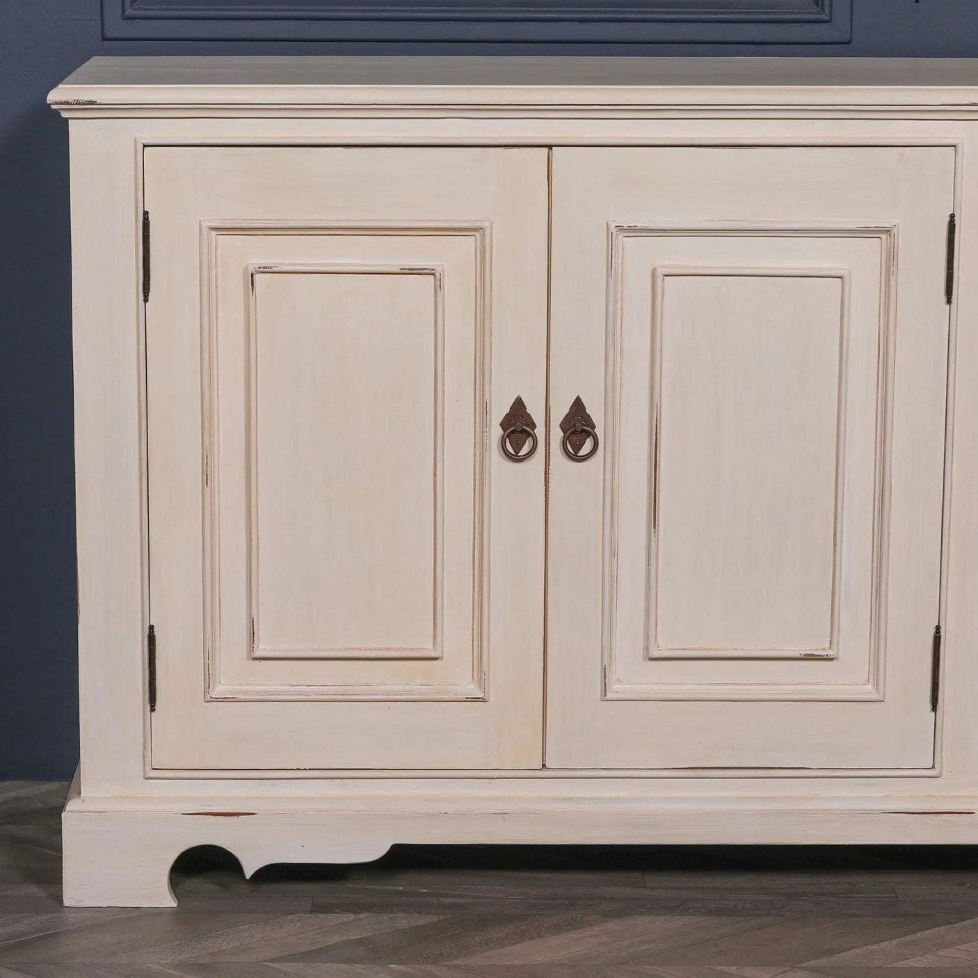 Cream wood sideboard cabinet with paneled doors and metal ring handles on wood floor